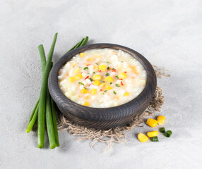 Vegan chowder soup made of rice, corn, potatoes, carrots, paprika with oatmeal cream in a wooden bowl in rustic style on a light gray background