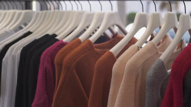 Close-up of woman's hand picking sweater from fashion boutique rack