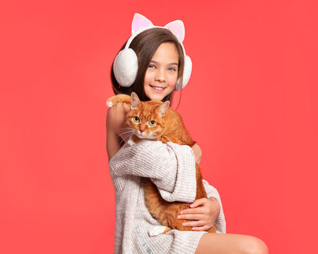 Cute European teen girl and red cat. A child and a cat on a red background. Pets, care for the animals. Cat care, veterinary medicine, animal feed.