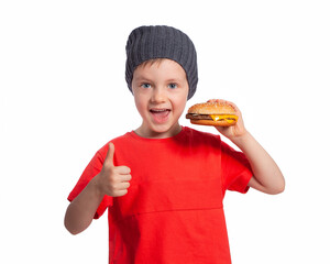 A child with a hamburger shows the class gesture. A beautiful European boy is going to eat fast food. Happy child. A cheeseburger snack. Favorite children's food.