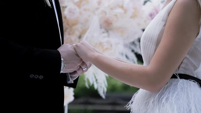 The bride and groom hold hands on the background of the wedding arch for the ceremony of exchange of rings. up summer day no face. luxury lifestyle. Bridal fashion.