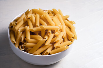 Raw dry uncooked penne pasta noodle in a bowl on white background 