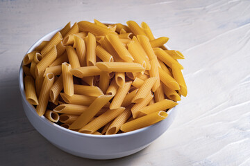 Raw dry uncooked penne pasta in a bowl on white background. Good for basil tomato pesto sauce Homemade fresh Italian food style bio organic whole wheat vegan spaghetti noodle for a healthy meal
