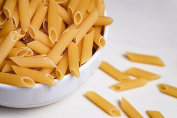 Raw dry uncooked penne pasta noodle in a bowl on white background 