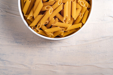 Raw dry uncooked penne pasta noodle in a bowl on white background 