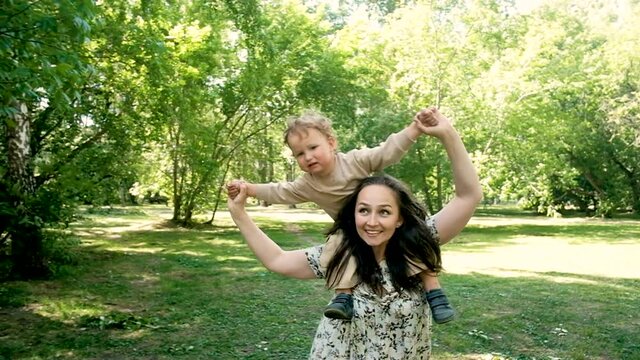 young beautiful mother holds a 2 year old sweet son. Walk in the summer in the park. . carries on the shoulders a close-up