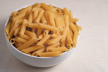 Raw dry uncooked penne pasta in a bowl on white background. Good for basil tomato pesto sauce Homemade fresh Italian food style bio organic whole wheat vegan spaghetti noodle for a healthy meal