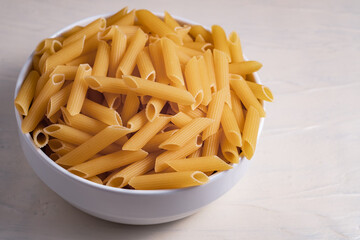 Raw dry uncooked penne pasta noodle in a bowl on white background 