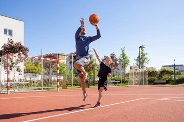 Father and son playing basketball barefoot on a playground