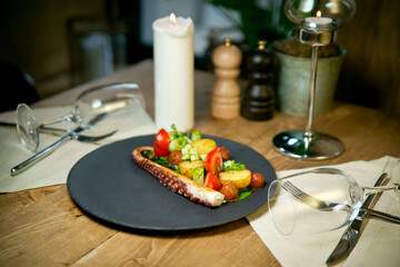 Octopus tentacles with baked potatoes and vegetables .On black plate. On a rustic wooden background