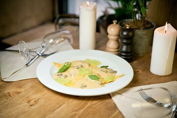 Lamb Ravioli and cheese sauce and chanterelles. On a white plate. against the restaurant background