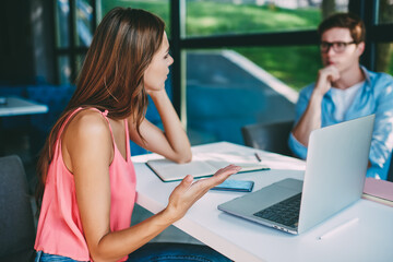 Cheerful young man and woman watching funny webinar on netbook in cafe