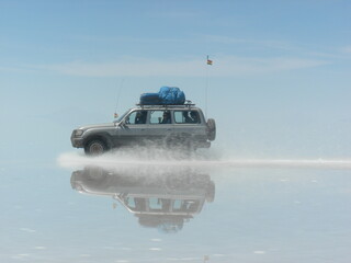 jeep car driving through the Salt Flats in Bolivia. It's rainy season and a perfect reflection of...