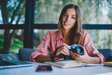 Positive young woman photographer making setting of lenses in coworking space