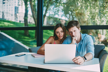 Cheerful young man and woman watching funny webinar on netbook in cafe