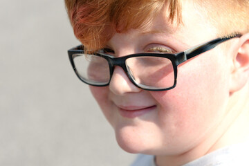 Portrait of a cute red-haired boy wearing glasses smiling and looking into the lens. Cute smiling red-haired boy with eyeglasses.