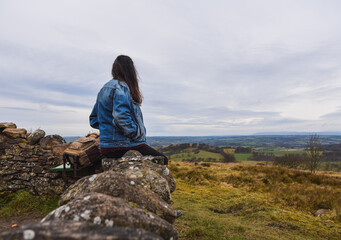 Unrecognizable girl wearing a blue denim jacket sitting in a rock in a nature background