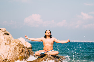 Man meditating on a rock at the sea