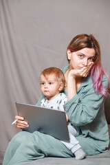 A young woman works at home with a tablet computer, along with a child.the son wants to communicate...