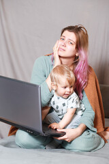 Stay at home, mom works remotely on a laptop, taking care of her child. A young mother on maternity leave is trying to work as a freelancer with a baby.