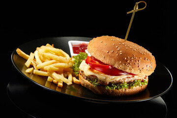 Big fresh burger with sauce and fries on black plate isolated on black background.  American classic burger menu.