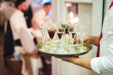 Waiter carrying tray with several various alcoholic drinks. Man serving beverages. Celebration, birthday, party, wedding concept.
