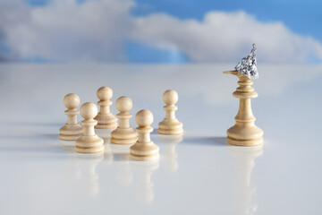 Chess piece king or queen with tin foil helmet and long lying nose stands in front of small game pieces, conspiracy theory concept, bright ground and very blurry sky with clouds, copy space