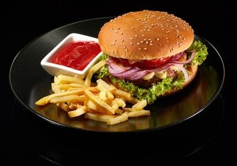 Big fresh burger with sauce and fries on black plate isolated on black background.  American classic burger menu.