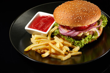Big fresh burger with sauce and fries on black plate isolated on black background.  American classic burger menu.