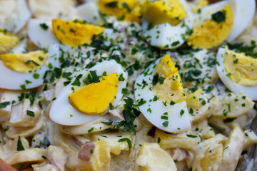 Potato salad with cooked eggs and herbs garnish, full frame close-up shot, selected focus