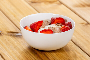 Fresh strawberries with ice cream in a glass vase on a wooden background close-up. Copy space