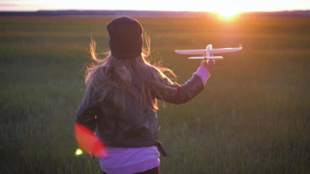 Happy little girl playing with a airplane in the meadow during sunset. Concept big child dream.