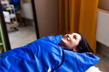 Woman in blue pressotherapy suit lying down having pressure therapy for weight loss in spa salon. Doctor help lose weight and slimming