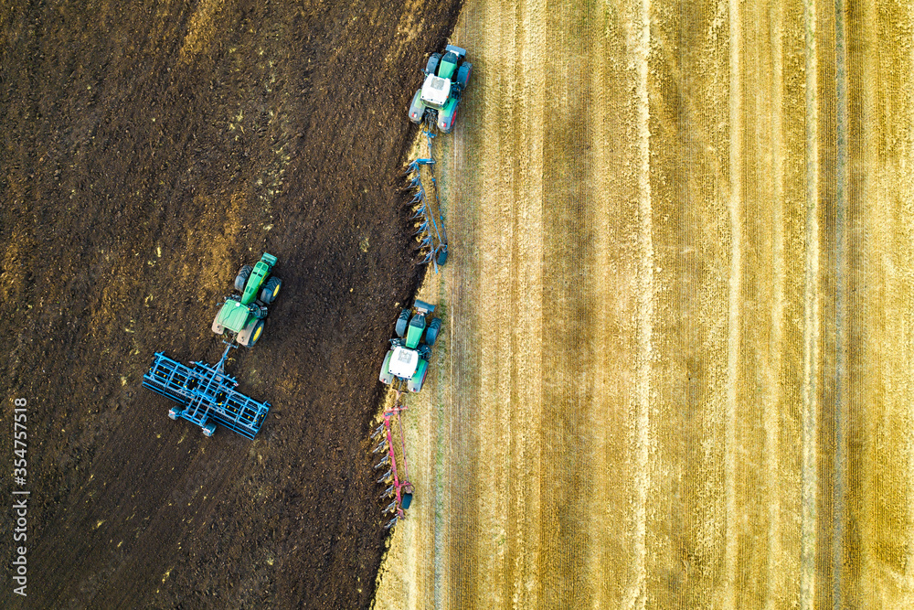 Wall mural Aerial view of a tractor plowing black agriculture farm field after harvesting in late autumn.