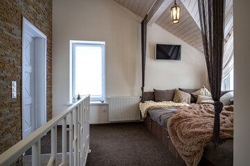 Interior of a modern house spacious hallway with big soft resting place. Contemporary wide sofa with many pillows and light window onder wooden loft ceiling.