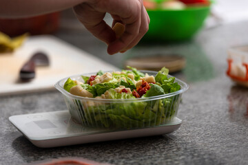 hand putting ingredients into a salad on plastic tray for delivery