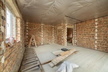 Interior of unfinished brick house with concrete floor and bare walls ready for plastering under construction. Real estate development