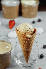 ice cream in a waffle cone on a light background. The ice cream is melting. Waffle cones and strawberries in the background