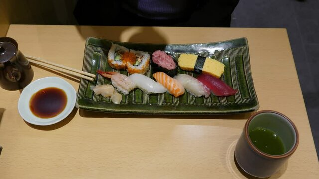 Assorted sushi on platter, tourist woman take cup with miso soup, top-down view of table at Japanese restaurant. Basic set meal served at affordable eatery in Tokyo