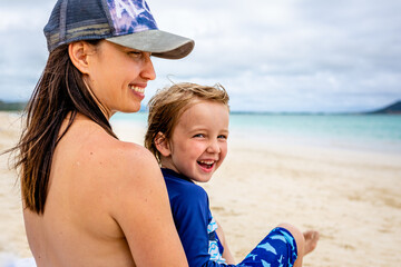 Mother and son enjoy looking out at ocean while sitting on beach together
