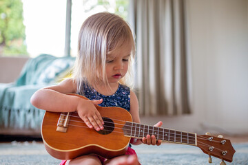Young caucasian girl learns to play guitar or ukulele