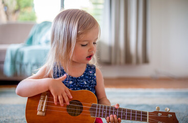Young caucasian girl learns to play guitar or ukulele