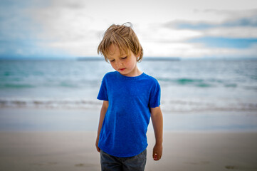 Young boy stands on beach in deep thought