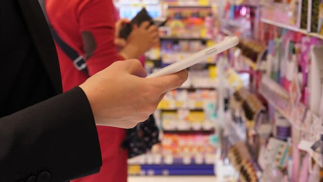 Woman texting using phone, stay against shelf with skin care productions at Japanese beauty supply store. Close up shot with blurred background. Tourist girl during shopping