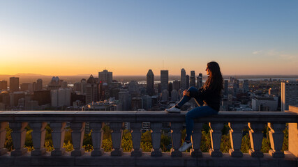 Montreal, Canada - may 2020 : young woman sitting on the Kondiaronk belvedere's stone wall and admiring the sunrise