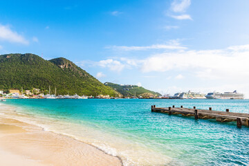 Philipsburg, Sint Maarten. View from Great Bay Beach of Royal Caribbean and Norwegian Cruise Line ships docked in port near coastline mountains. Scenic tropical vacation setting.