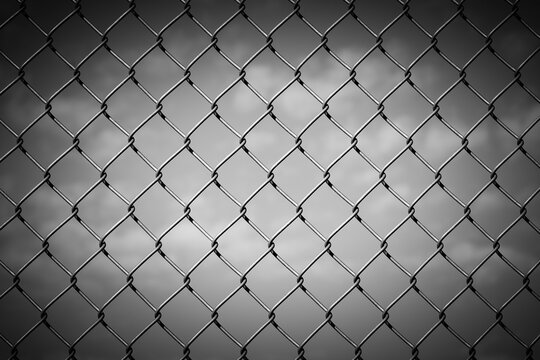 Black and White Image of a Chain Link Fence against a Cloudy Sky