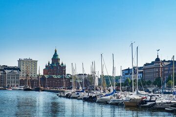 Fototapeta na wymiar Scenic Finnish cityscape of Scandinavian Old Town pier with Uspenski Cathedral, old boats and sailing ship in sea harbor. Katajanokka district is famous tourist destination in Helsinki city, Finland