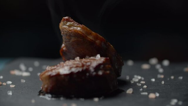 Close up of beef steak rotating on black background in slow motion. Female hand putting microgreen on filet mignon