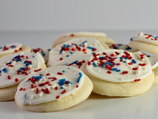 Sugar cookies with white frosting and red, white and blue sprinkles for the 4th of July, Memorial Day, Veteran’s Day and anything patriotic on a white background.  Delicious festive dessert.